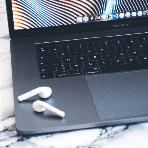 image of the front left corner of an Apple laptop showing part of the screen, keyboard, and trackpad with AirPods sitting next to the trackpad
