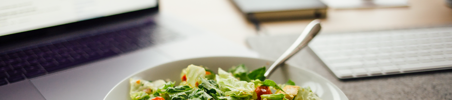 image of salad in white ceramic bowl with fork front of a laptop