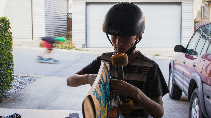 child standing in garage with his skateboard next to a car that was backed in