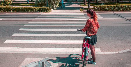 image of a young with her bike waiting to cross the street at a crosswalk