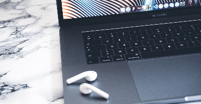 image of a apple laptop with earbuds lying on it, focus is on the keyboard and mouse pad